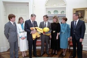President Ronald Reagan During Photo Op with Al Unser Jr., Bobby Unser, Al Unser Sr., Karen Unser, Shelley Unser, and Marsha Unser and Receiving Gifts of a Helmet and Jacket and Book in The Oval Office, 1/23/1986.