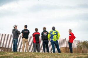 Group observes from behind the fence at a dirt track event.