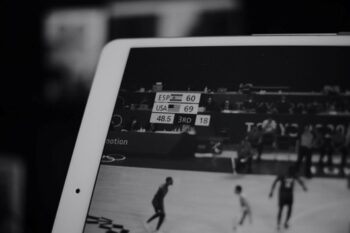 A black and white close-up of a tablet screen showing a basketball game with a live score graphic